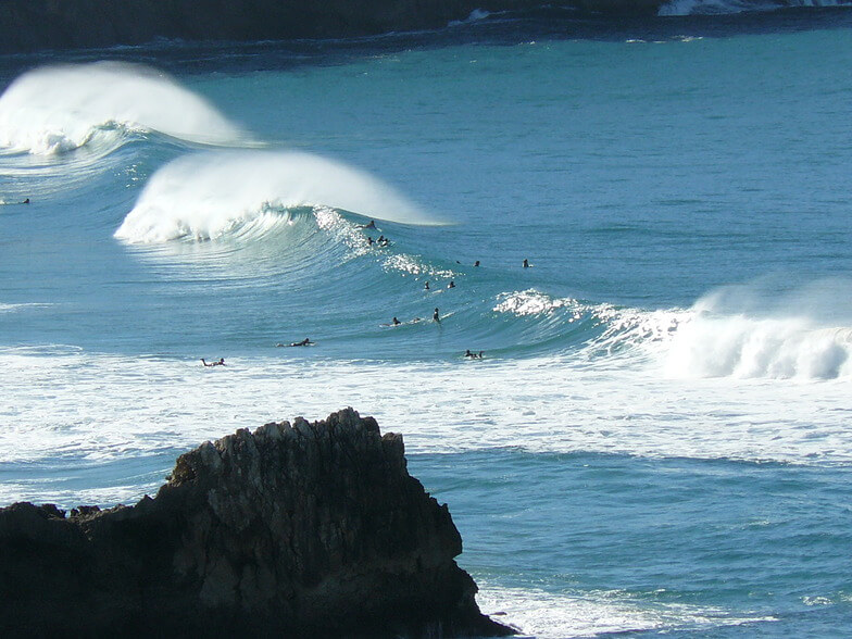 Ocean surfers catching waves along the sandy shore break of Praia do Tonel backed by steep cliffs
